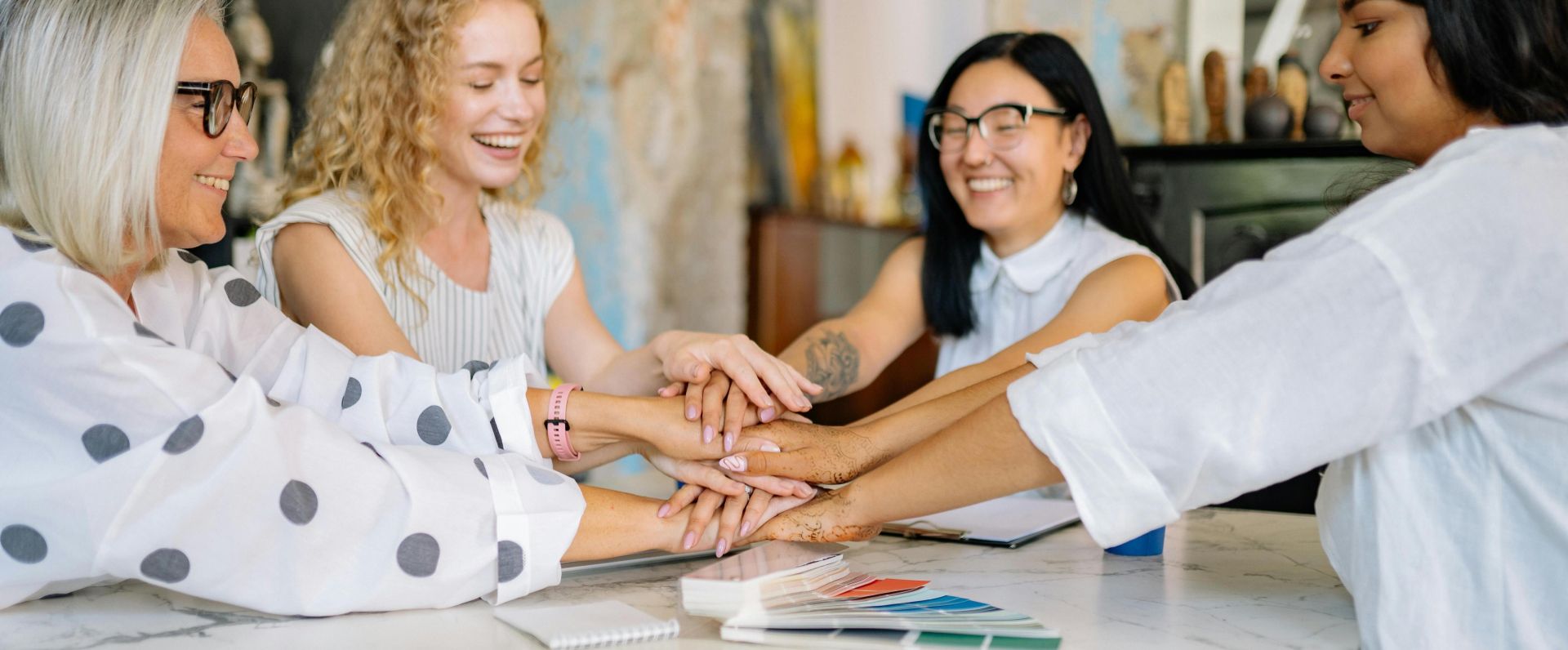Diverse group of businesswomen collaborating at a desk, embracing teamwork with smiles and positivity.
