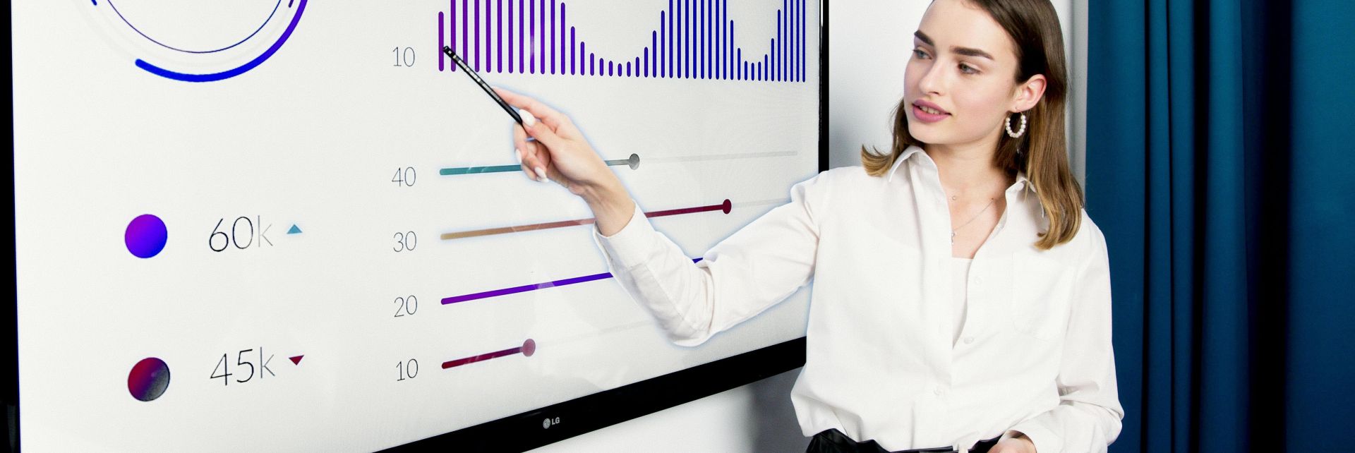 Businesswoman presenting data on a large digital screen in a modern office setting.